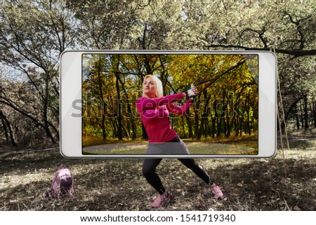 Young woman exercising in autumn park, saturated image in smartphone s camera