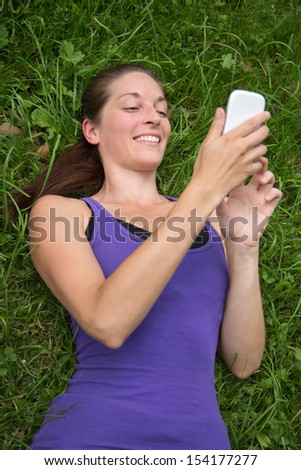 Young happy woman lying on a green meadow is using a smartphone