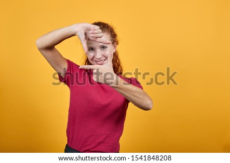 Young European woman showing gesture with her hands. Charming girl over isolated yellow background wearing pinky T-shirt and black jeans. Gorgeous lady having beautiful grey eyes.