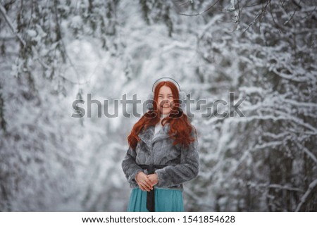 photo session for a beautiful red-haired girl who walks through a snowy forest