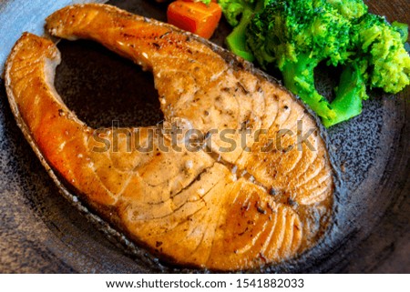 fried salmon steak with carrots and broccoli on a tiled dish.