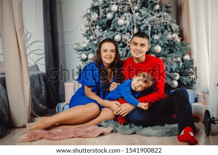 Family, dad, mom and little son are sitting under the Christmas tree with gifts indoors. Christmas concept, gifts, memories of childhood.