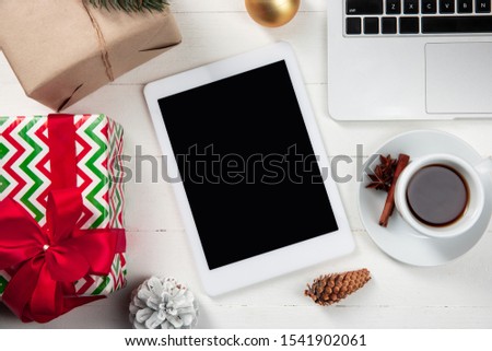 Mock up blank empty screen of tablet on the white wooden background with colorful holiday's decoration, tea and gifts. Copyspace, negative space for your advertising. 31 of December, New Year concept.