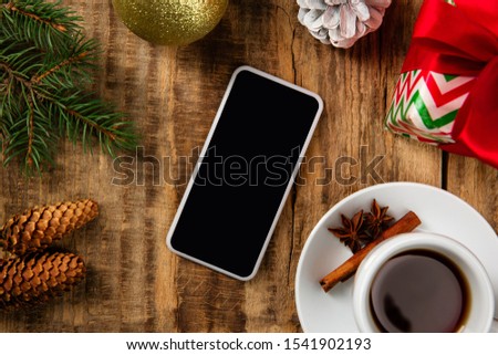 Mock up blank empty screen of smartphone on the wooden background with colorful holiday's decoration, tea and gifts. Copyspace, negative space for your advertising. 31 of December, New Year concept.
