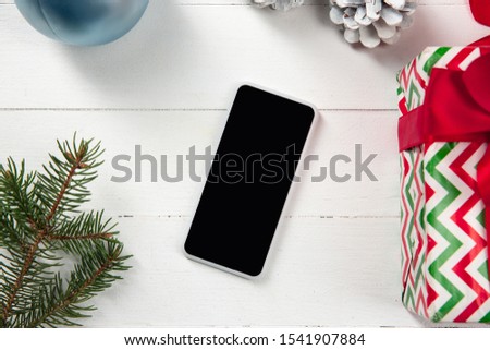 Mock up blank empty screen of smartphone on the white wooden background with colorful holiday's decoration and gifts. Copyspace, negative space for your advertising. 31 of December, New Year concept.