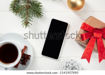 Mock up blank empty screen of smartphone on the white wooden background with colorful holiday's decoration and gifts. Copyspace, negative space for your advertising. 31 of December, New Year concept.