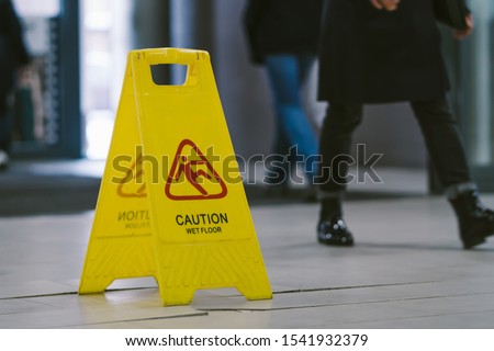 Yellow caution wet floor sign on broken mall floor tiles and feet walking girl.