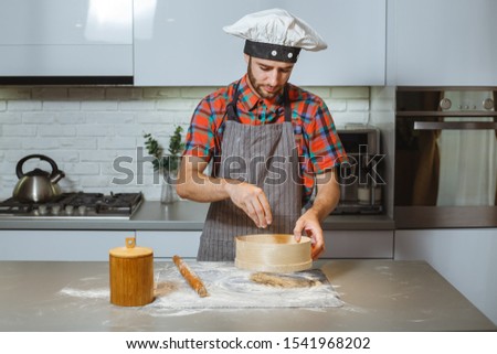 Young man sifting flour from old sieve onto old wooden kitchen table.