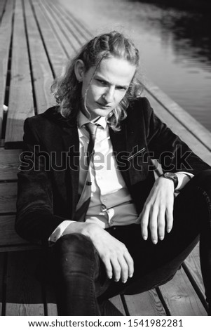  A portrait of a young man in a suit and red tie sitting on a wooden bridge, black and white photo
