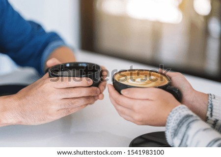 Closeup image of a man and a woman holding two coffee cups together