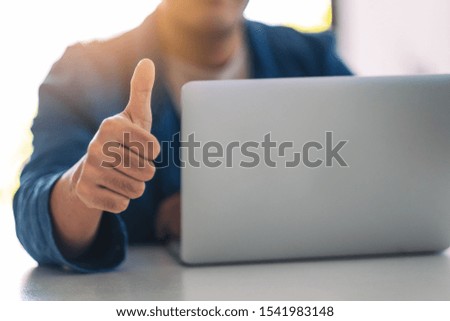 Businessman showing thump up while working on laptop in office