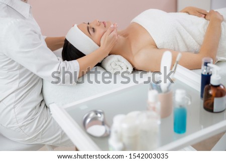 Charming young woman lying on daybed and having face massage stock photo