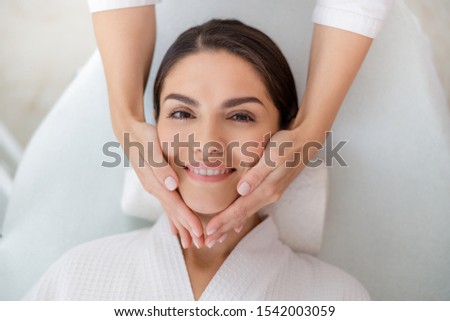 Masseuse hands massaging face of joyful young woman stock photo