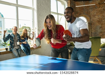 Young people playing table tennis in workplace, having fun. Friends in casual clothes play ping pong together at sunny day. Concept of leisure activity, sport, friendship, teambuilding, teamwork. Royalty-Free Stock Photo #1542028874