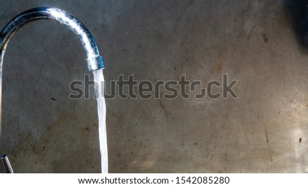 The water tap that was opened had water flowing behind it, a cement wall.