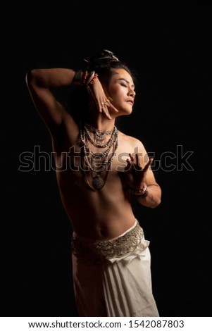 Beautiful Asian wearing traditional dress outfit does a dramatic dance move against a black background