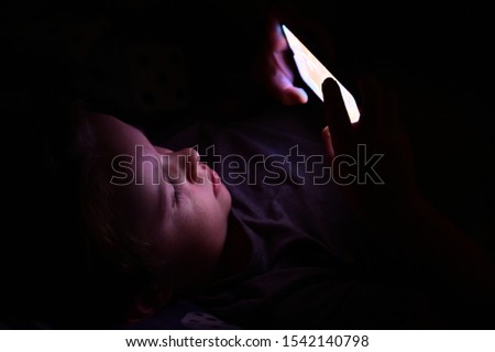 A photo of a child in an apartment sitting in front of a screen playing a game. at night. Concept new technologies, the impact of the Internet on children.