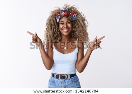 Cheerful friendly, optimistic african american woman with blond curly-haired afro hairstyle, headband, pointing sideways, different directions left right, smiling happy, delighted, white background