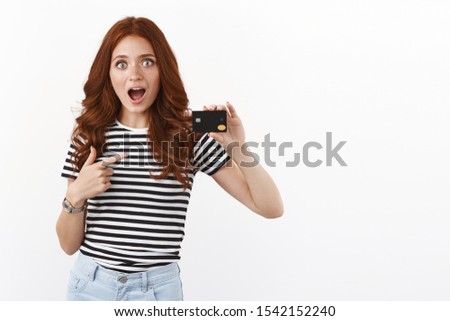 Surprised and impressed speechless cute redhead female student, pointing black credit card, staring amazed and astonished, explain cool banking offers, open deposit, have big cashback