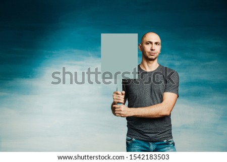 Attractive bald man in a T-shirt with a protest poster in his hands on a blue background.