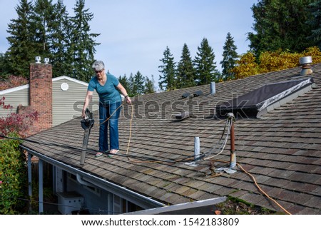 Rooftop view of suburban home, mature woman with leaf blower cleaning roof and gutter
 Royalty-Free Stock Photo #1542183809