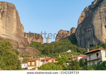 Houses and church in foothills among trees in valley below towering converging rocks and pinnacles at Meteora,Greece.