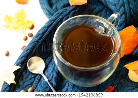 Cup of coffee with a heart shape on a warm knitted plaid background with autumn leaves.