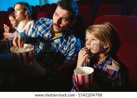 Young caucasian family watching a film at a movie theater, house or cinema. Look expressive, astonished and emotional. Sitting alone and having fun. Relation, love, family, childhood, weekend time.