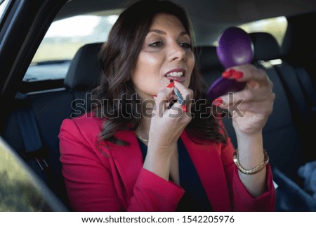 A middle-aged businesswoman repairs makeup in a car.Stock photo