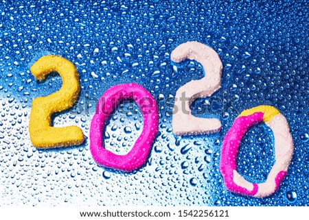 2020 New year design concept. Colored figures of plasticine on a blue background with water drops.