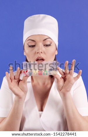 young woman doctor in a white coat and hat with pills and capsules in hands posing on a blue background