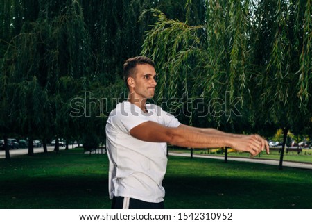 Full-length photo of a handsome, strong male stretching on a grass and on a natural background. Workout in the outdoors