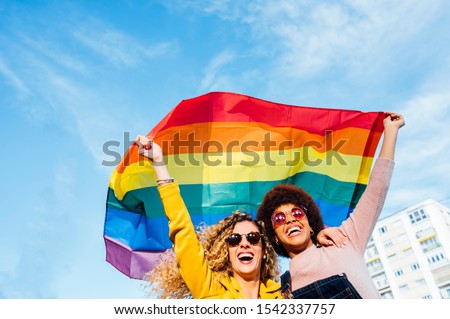 Two women friends hanging out in the city waving LGBT with pride flag Royalty-Free Stock Photo #1542337757
