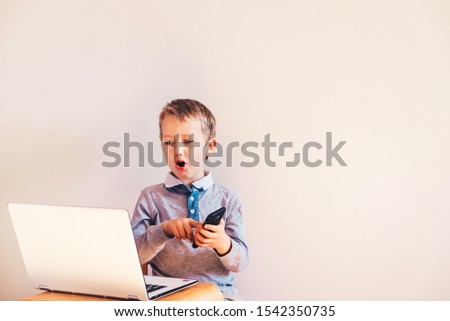 Young boy using a laptop while talking on mobile phone doing business.