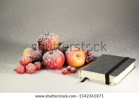 ripe beautiful apples and fruits lie on a gray background, in the snow, with a Christmas ball, with a candle, notebook, berries, snowman, garland, iris, rose hips
