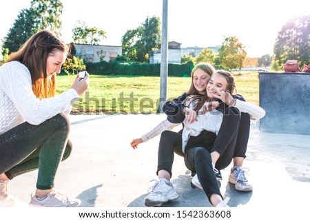 Three girls schoolgirls teenagers 12-15 years old, ride skateboard, take selfie pictures on phone. Emotions of joy fun enjoyment, happy are smiling, casual clothes, relaxing after school on vacation.