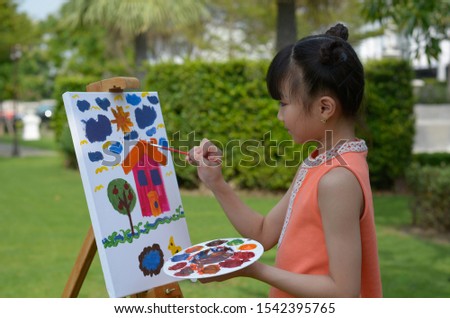 The Young Asian girl is enjoying painting color on white canvas in the front yard.