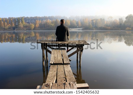 a man is sitting on the bridge. melancholy. rest at nature. peace of mind and quiet on the lake. breathe deeply away from the bustle of the city. Indian summer
