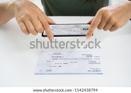 Woman Taking Photo Of Cheque To Make Remote Deposit In Bank Royalty-Free Stock Photo #1542438794