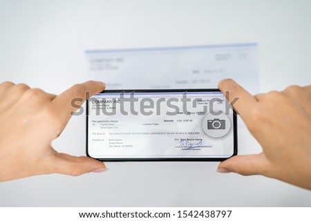 Woman Taking Photo Of Cheque To Make Remote Deposit In Bank Royalty-Free Stock Photo #1542438797