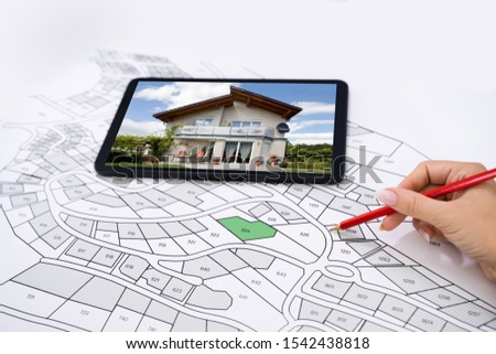 Hand Holding Pencil Over Cadastre Map New Tablet With House Photo