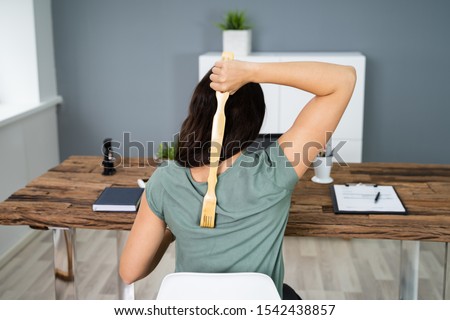 Young Woman Using Back Scratcher At Office Royalty-Free Stock Photo #1542438857