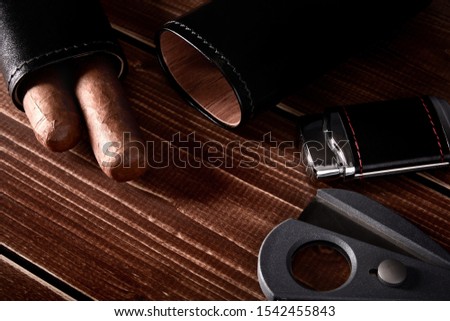 Still life with cuban cigars in black leather case, cutter and lighter on old wooden table top with space for text Royalty-Free Stock Photo #1542455843