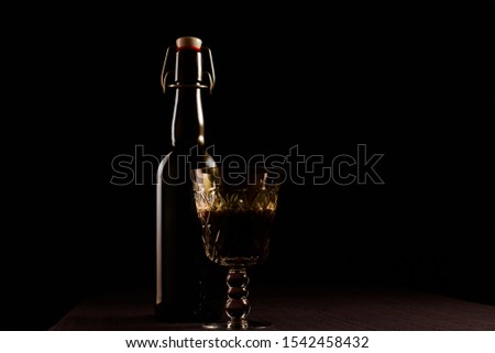Bottle with alcoholic drink corked up. A glass with alcohol standing on a table laid by a cloth. Light patches of light on objects. The intimate atmosphere, the twilight at restaurant.Reflections.