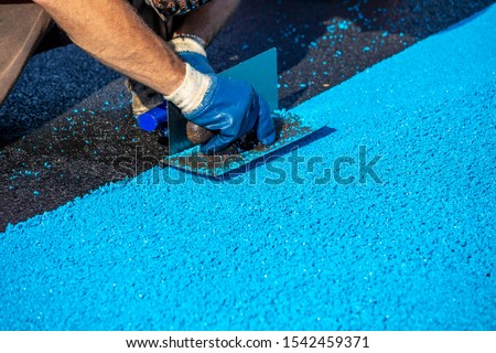 Mason leveling artificial rubber coating for playgrounds and  sports, applied on the surface by a steel trowels. PDM rubber granules. Selective focus. Royalty-Free Stock Photo #1542459371