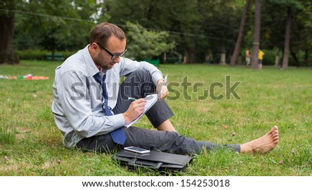 Businessman at the park with notes sitting on a grass.