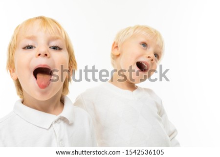 Little boys brothers with short light and red hair, blue eyes, cute appearance, in white jacket, light blue pants, stand and pose beautifully on camera and show tongues