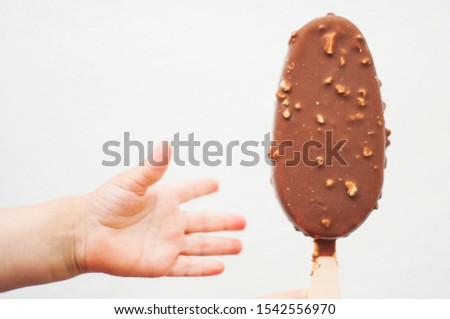 Small baby's hand reaching for the ice cream on a stick. Chocolate ice cream with nuts on white background.