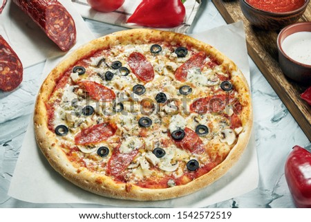 Homemade oven-baked pepperoni pizza with olives, blue cheese, salami, red sauce. Composition with crispy pizza, tomatoes on a light background. Copy space. Top view