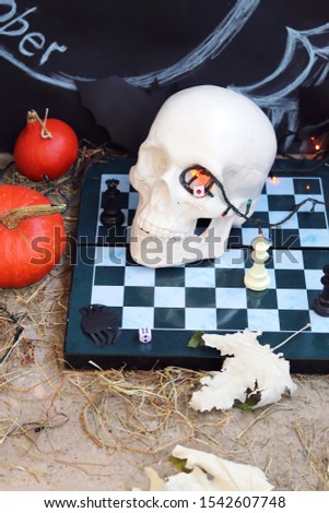 Halloween composition of skulls, autumn leaves, illuminations, mystical decor on a chessboard and concrete surface on a black background